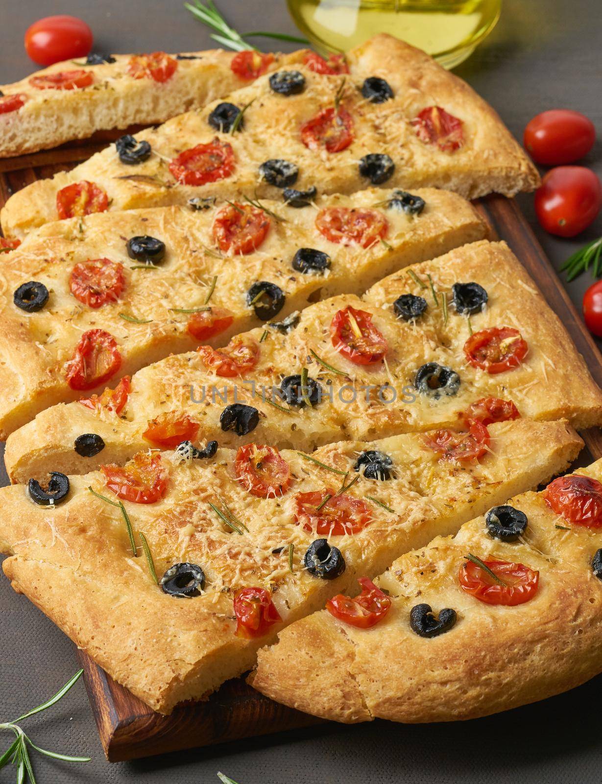 Focaccia, pizza, italian flat bread with tomatoes, olives and rosemary on dark brown table by NataBene