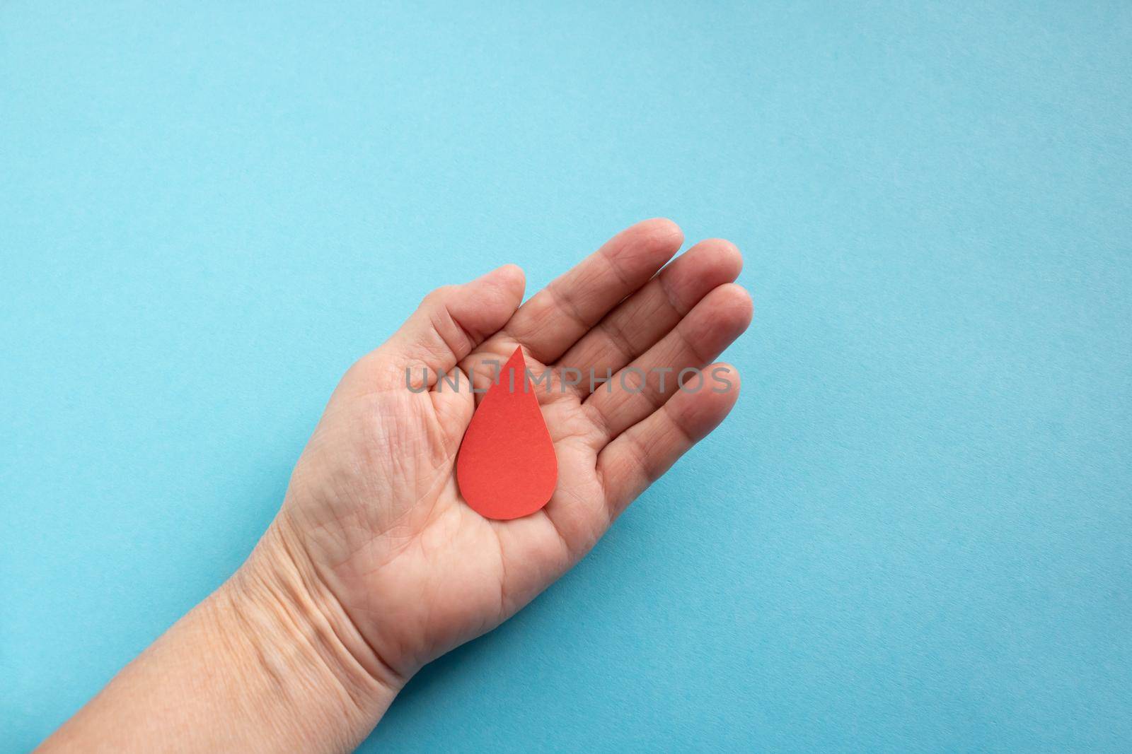The concept of the World Blood Donor and Hemophilia Day. Red paper drop of blood in the hand on a blue background by lapushka62