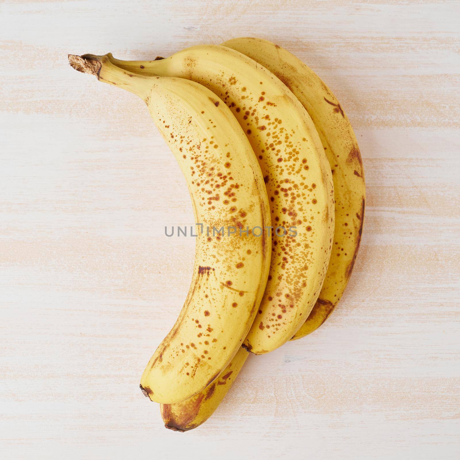 Ripe bananas with brown spots on a bright white wooden table
