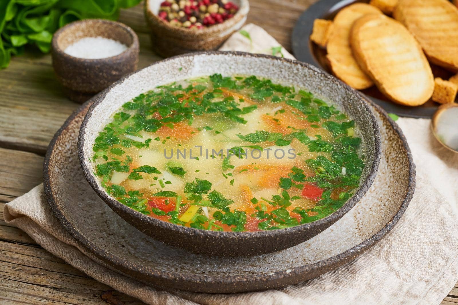 Rustic chicken soup with garnish, parsley, vegetables, homemade dish on the old dark table, side view