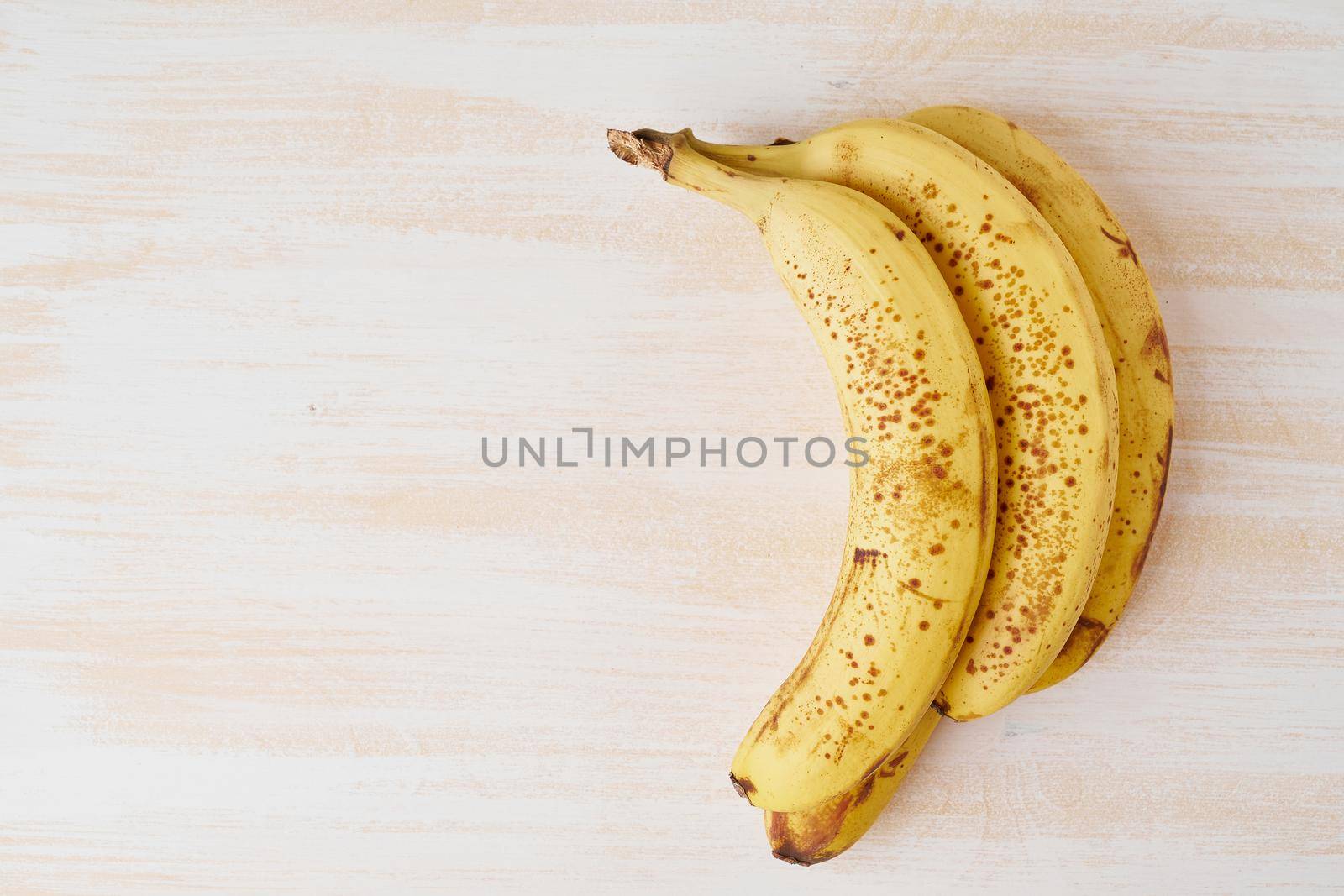 Ripe bananas with a brown spots on bright white wooden table, copy space, top view