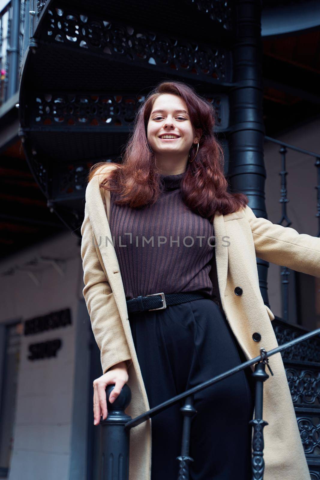 Beautiful serious stylish fashionable smart girl standing on a stairs and smiling, St. Petersburg city. Charming thoughtful woman with long dark hair, shooting from below, vertical
