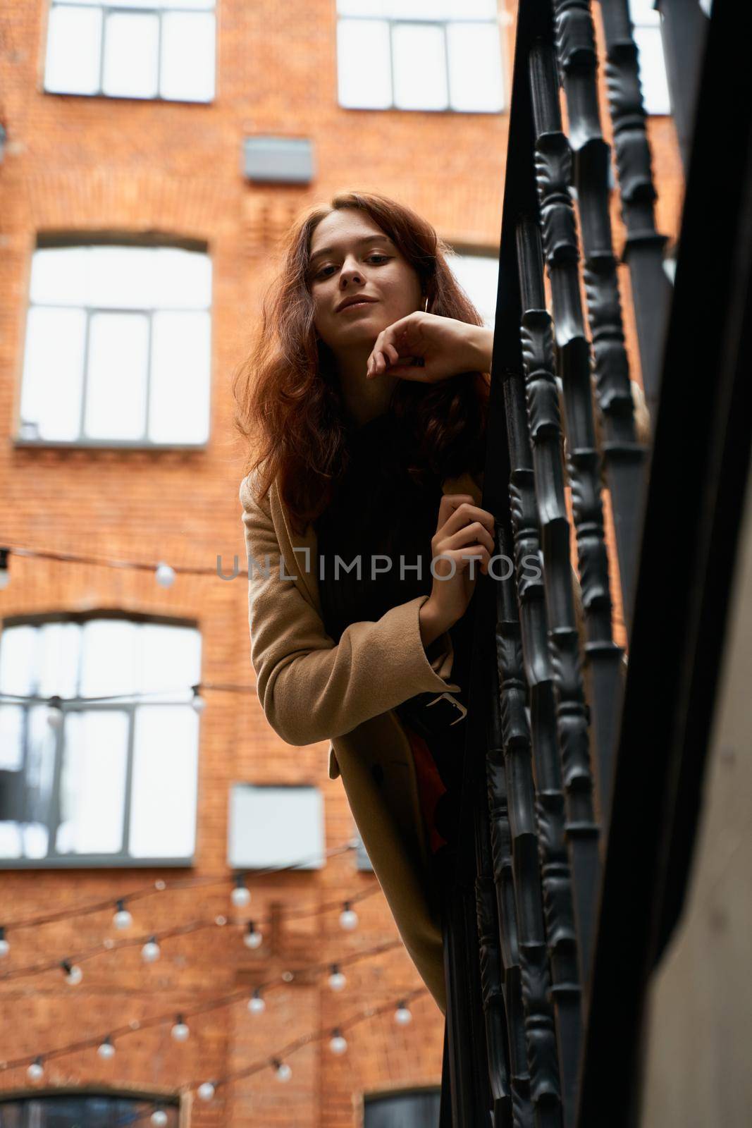 Beautiful serious stylish fashionable smart girl standing on the stairs, St. Petersburg city. Charming thoughtful woman with long dark hair, shooting from below, vertical