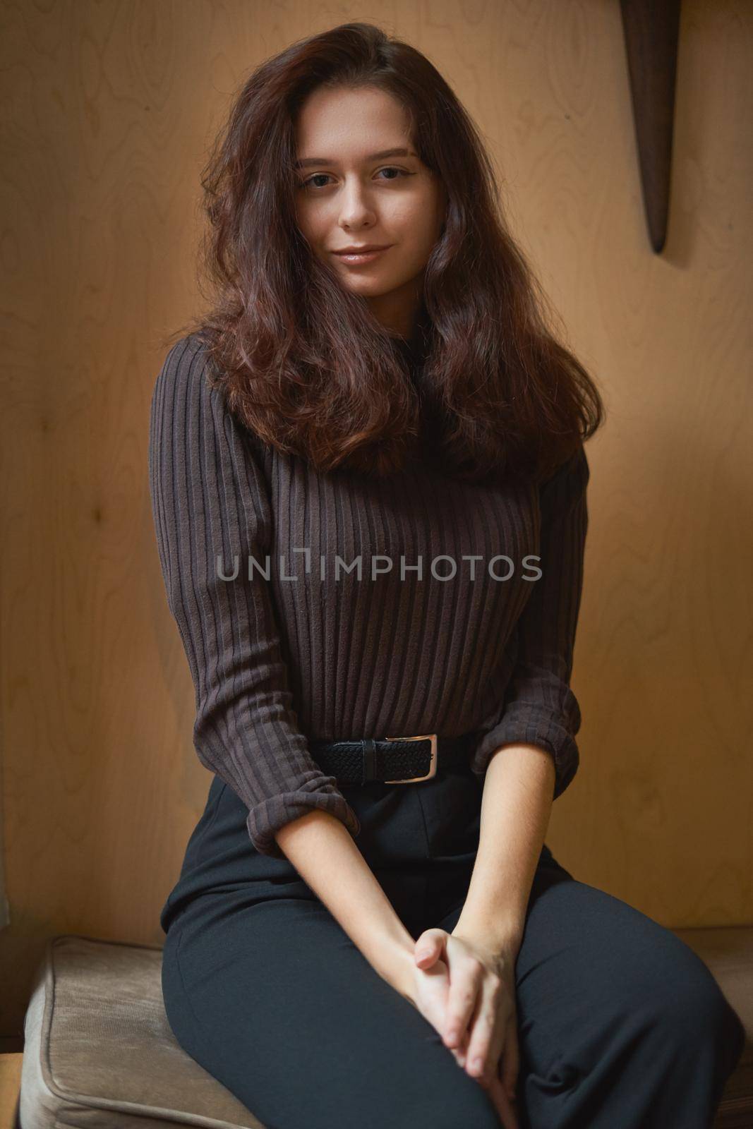 Portrait of beautiful intelligent brunette in the loft cafe. Charming thoughtful woman with long dark brown curly hair. Dark moody brown background, vertical