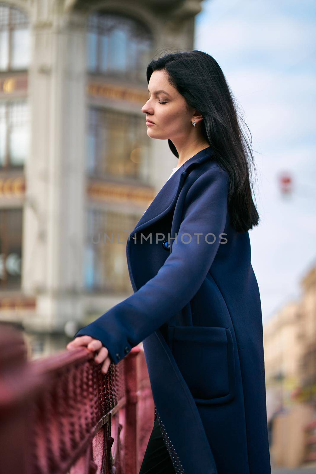 Portrait close-up of beautiful intelligent brunette who walks down street of St. Petersburg in city center. Charming thoughtful woman with long dark hair wanders alone, immersed in thoughts, vertical