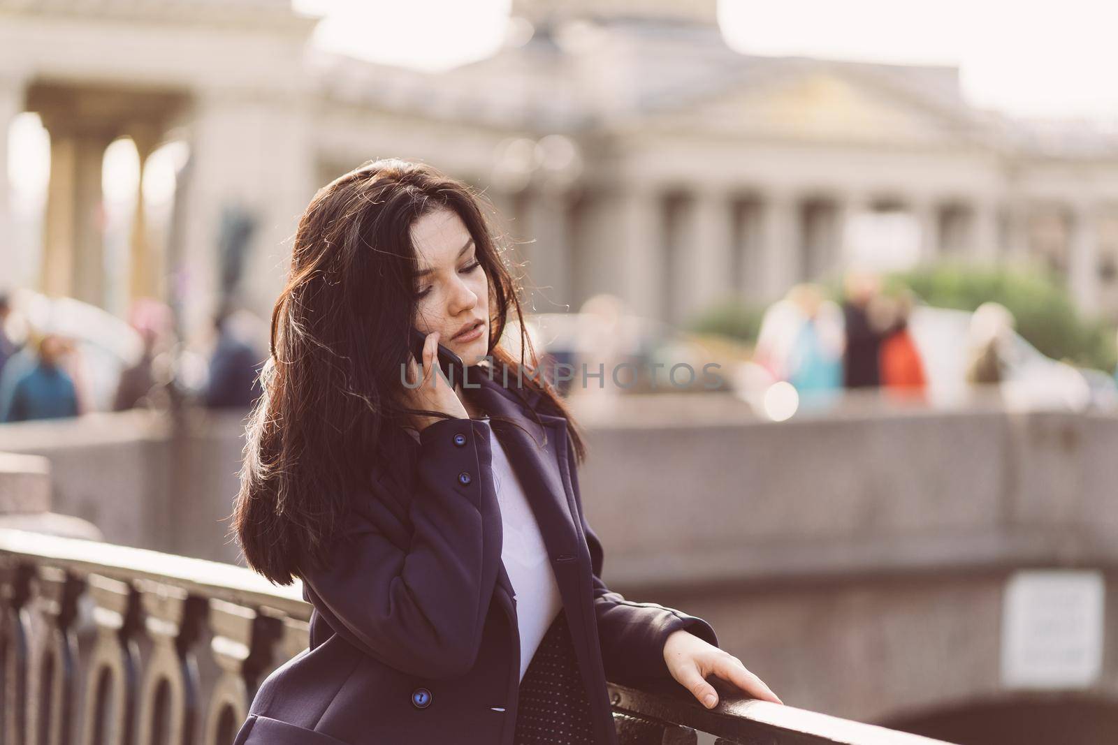 Woman with long hair talking on phone. Autumn or winter, girl in outdoor. Beautiful intelligent brunette in street of St. Petersburg in city center near bridge by NataBene