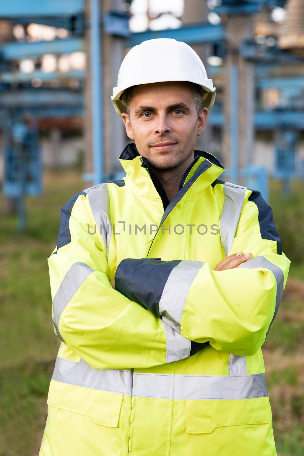 Portrait of industrial worker on power electric station. Portrait of happy male engineer in protective helmet crossing arms while looking to camera.