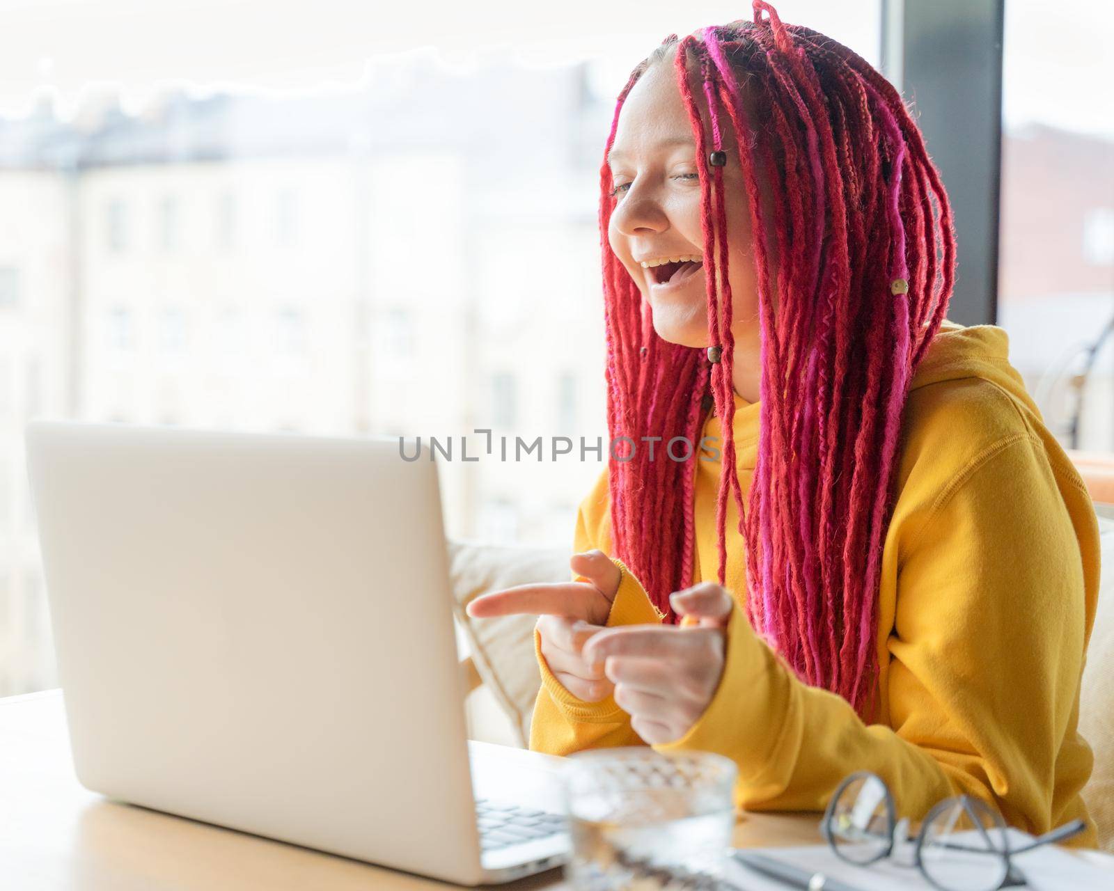 Woman looks at the laptop and laughs, says yeah. Online chat, stream. Girl with long pink hair, designer, creative specialist, freelancer, blogger. Concept of good luck, positive online communication