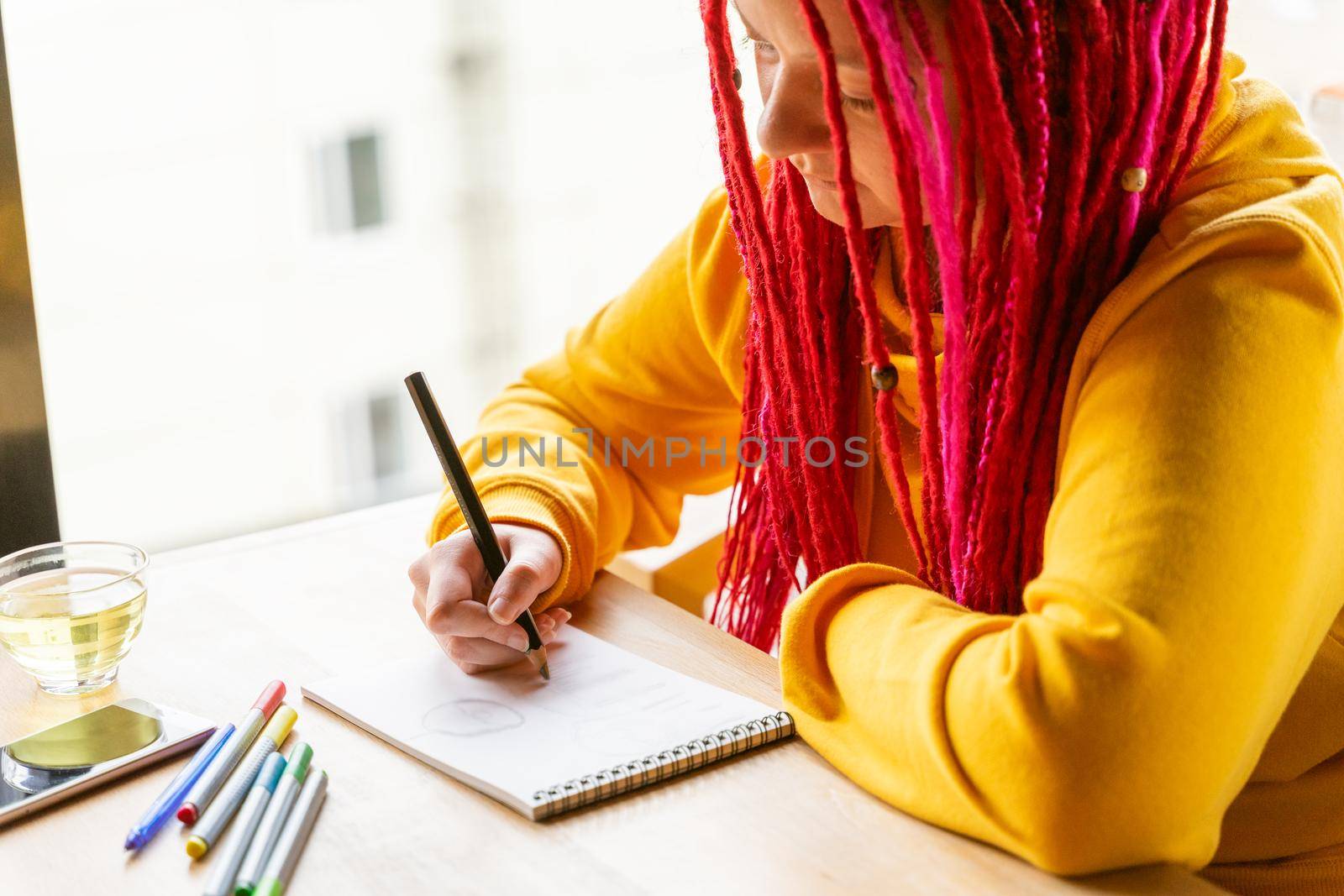 Girl sits in cafe and draws drawing with colored pencils and markers in notebook. Rest and relaxation, hobbies. The remote work concept of designer, illustrator, artist, close up