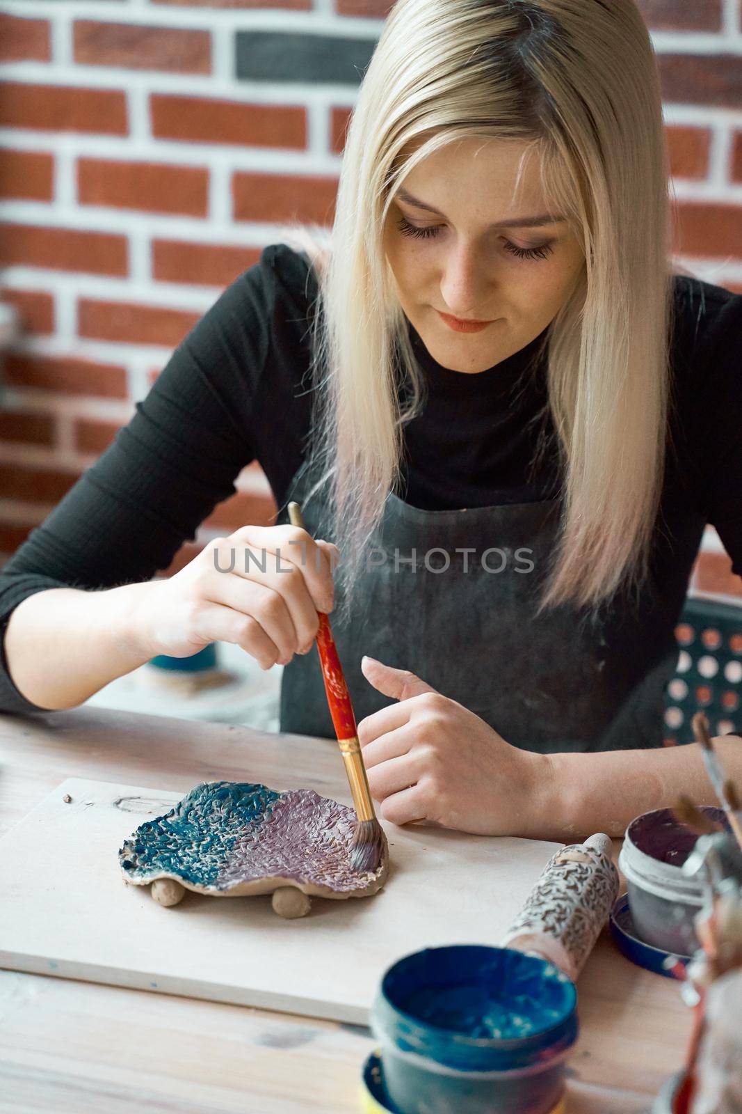 Woman making pattern on ceramic plate with paint brush. Creative hobby concept. Earn extra money, side hustle, turning hobbies into cash, passion into job, vertical by NataBene