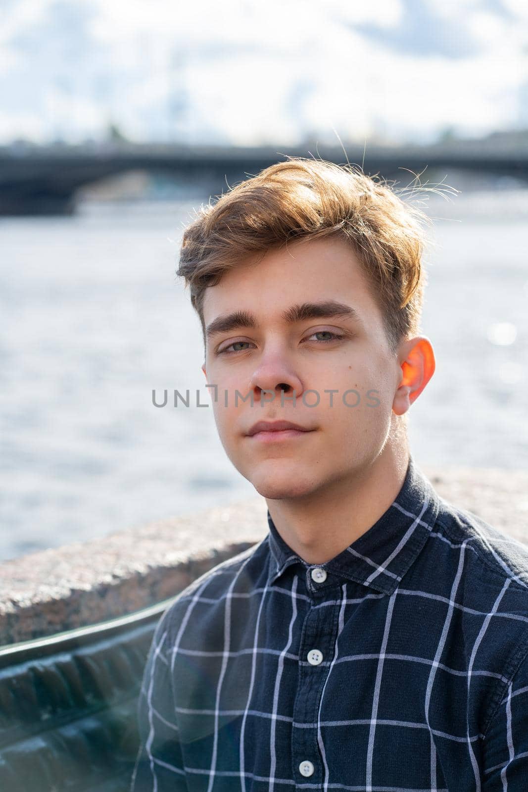 Portrait of a young guy, brunette with dark hair, Caucasian. Close - up of a guy, boy, man looking at camera. Outdoor in city by water