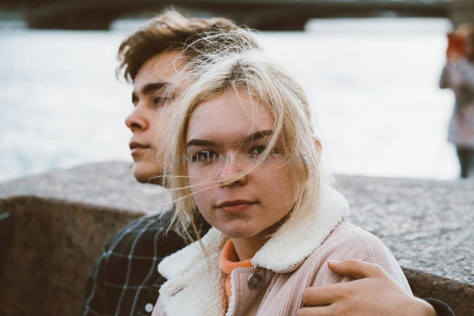 Teenagers in love sit on the waterfront in the city center, resting in autumn sun. Concept the first teenage love, the beginning of relations. A boy and a girl meet on a date, a couple. Girl close up