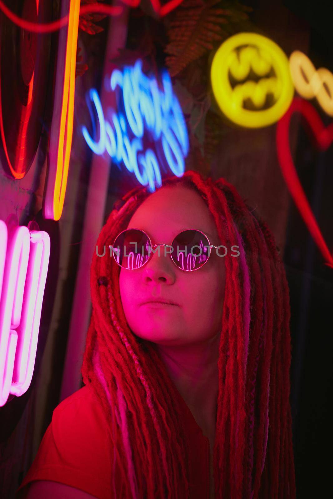 Girl in neon lights at party in nightclub, beautiful woman in sunglasses, with long pink hair, with dreadlocks pigtails, bright and stylish in the glow of neon signs, vertical, close up