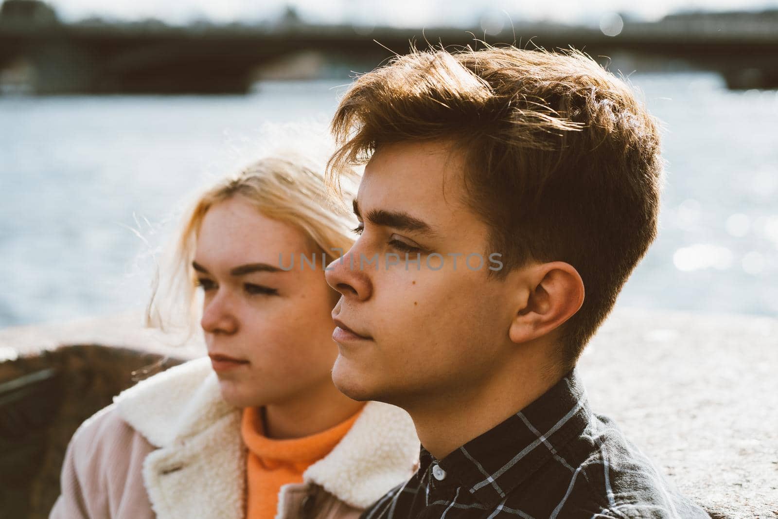 Teenagers in love sit on the waterfront in the city center, resting in the autumn sun. Concept the first teenage love, the beginning of relations. A boy and a girl meet on a date, a couple. Boy closeup