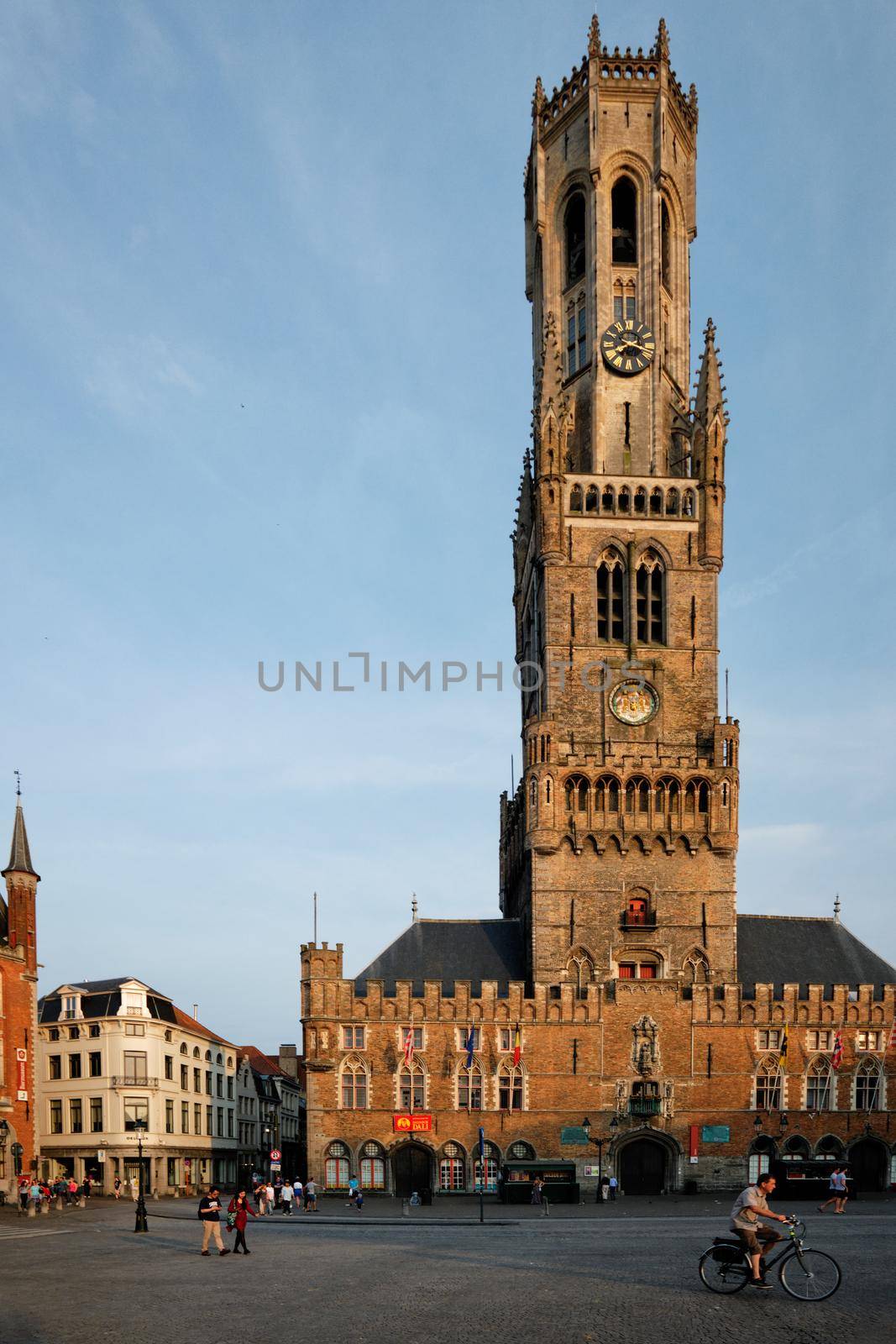 BRUGES, BELGIUM - MAY 28, 2018: Belfry tower famous tourist destination and Grote markt square in Bruges, Belgium with pedestrians and bicycle on sunset