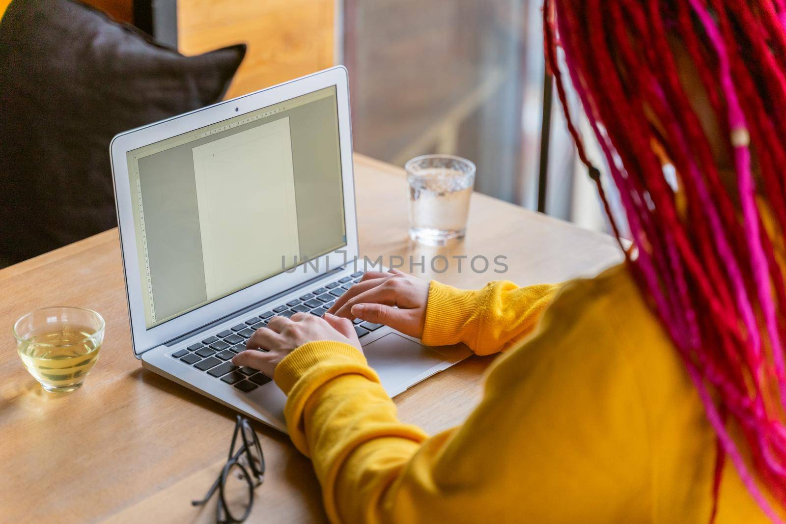 Concept of work of writer, journalist, blogger. Remote work, freelance. Bright beautiful young girl with long pink hair is typing on computer keyboard, blank white sheet