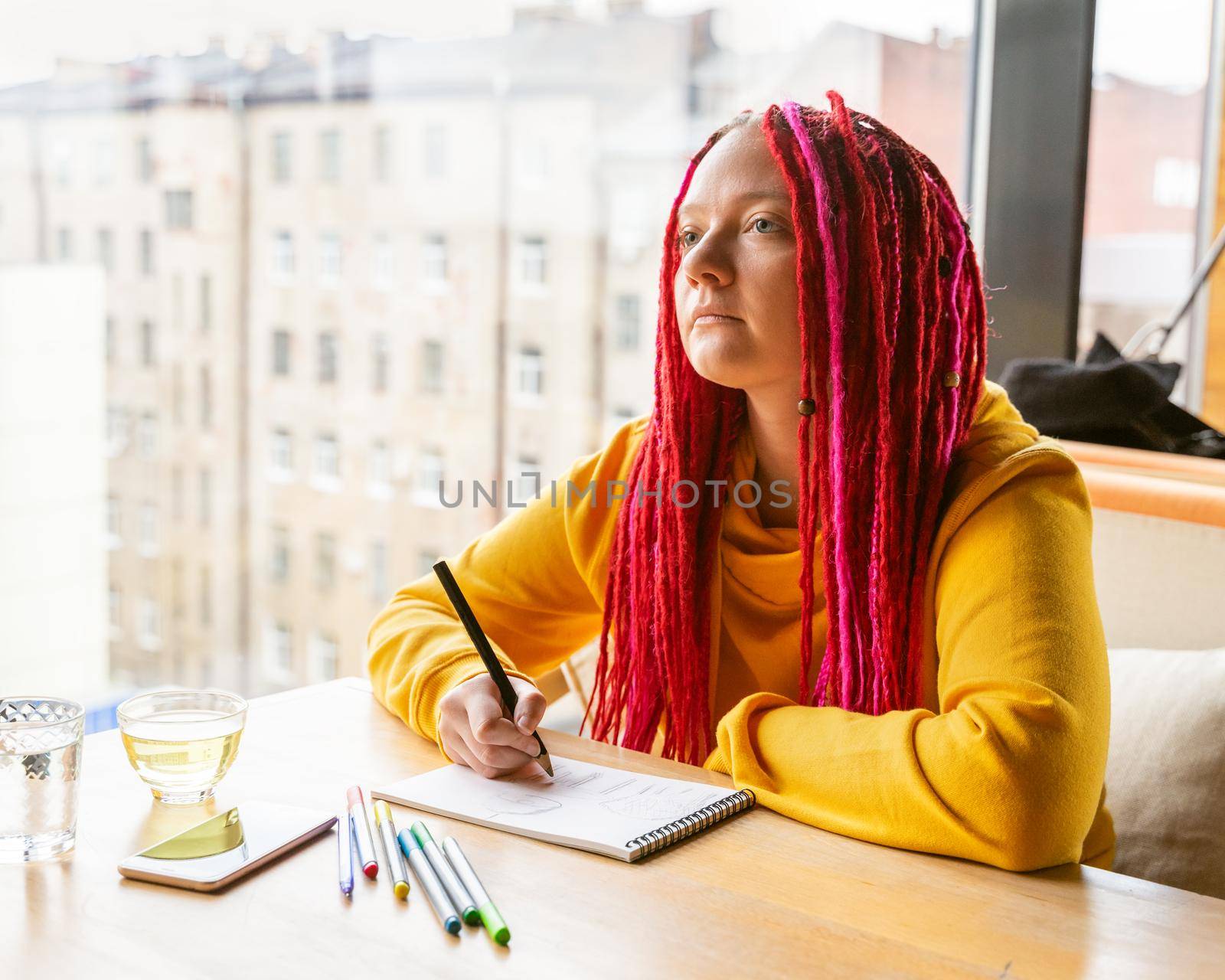 Girl sits in cafe and draws drawing with colored pencils and markers in notebook. Rest and relaxation, hobbies. The remote work concept of designer, illustrator, artist.