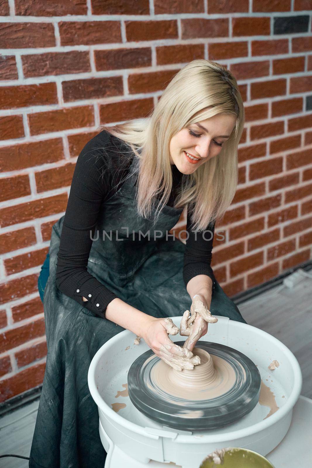Happy woman making ceramic pottery on wheel. Concept for woman in freelance, business, hobby. Earn extra money, turning hobbies into cash and passion into a job. Beautiful female smiling
