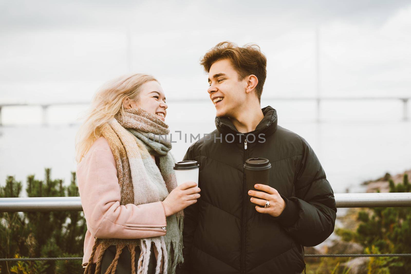 Lovely brunette guy and pretty girl blonde drink coffee and talking on a date. Loving teenagers are happy, smiling, laughing. Teen Love Concept. Outdoor.