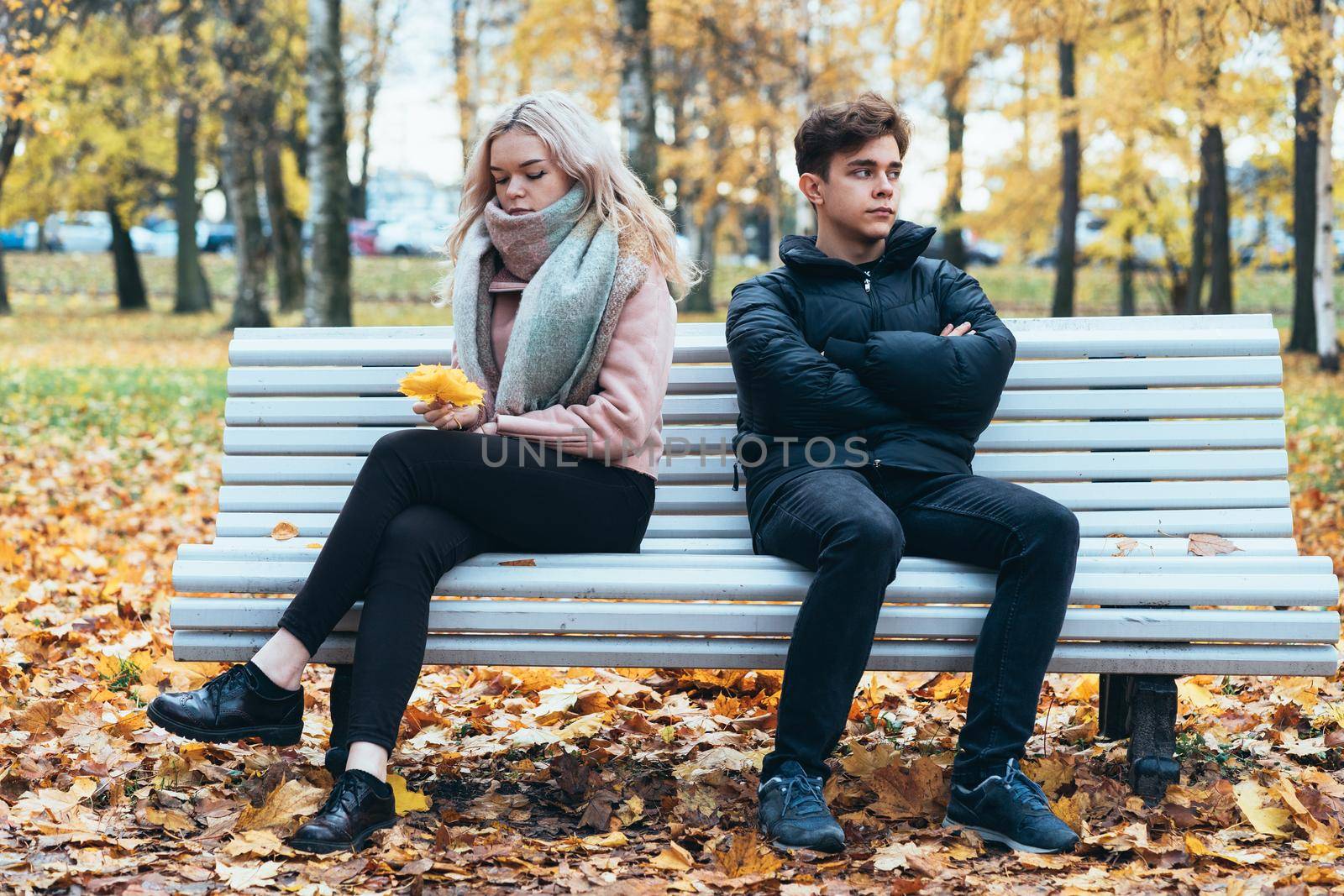 Two teenagers in love in quarrel. A brunette boy and blonde girl are sitting on opposite ends of benches, their backs to each other, do not want to talk and talk. Teenage Difficulty Concept