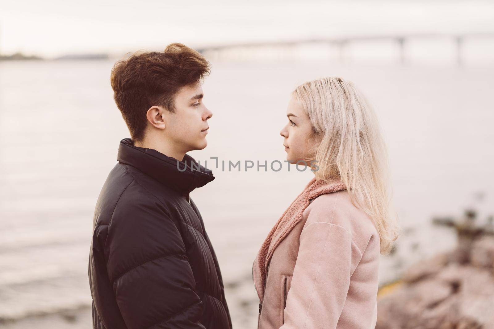 Lovely brunette guy and pretty girl blonde look at each other in the eyes, in love look. Loving teenagers are happy, smiling, kissing. Teen Love Concept. Outdoor.