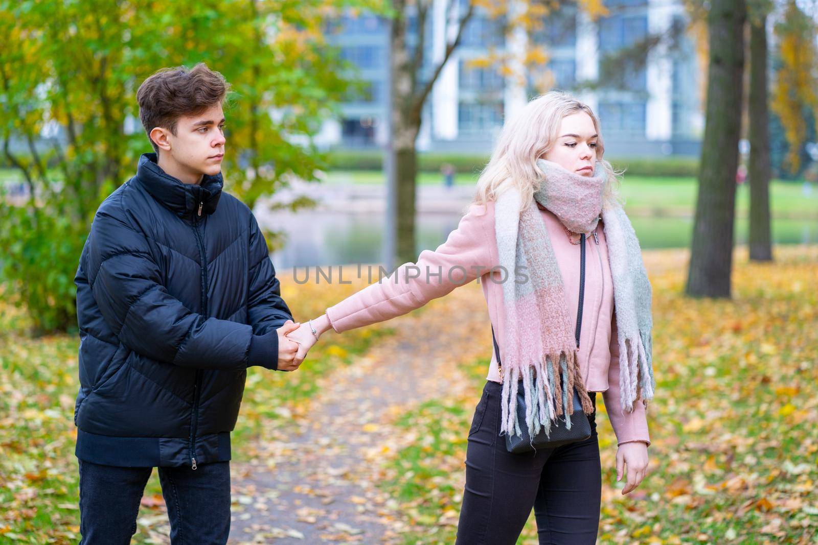 Two teenagers in love in quarrel. The blonde girl takes offense at boy, the guy holds her hand, asks the girl to stay and not leave. Concept of difficulties in adolescent relationships