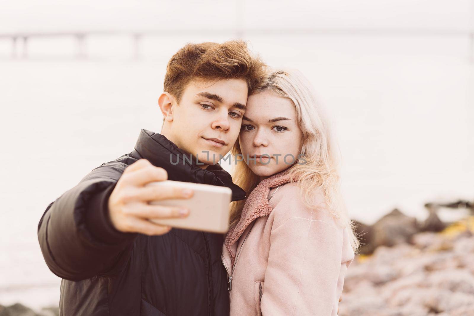 Loving teenagers on a date. Cute brunette boy and a beautiful blonde girl take selfie on cell phone. Concept of teen love, millennium generation