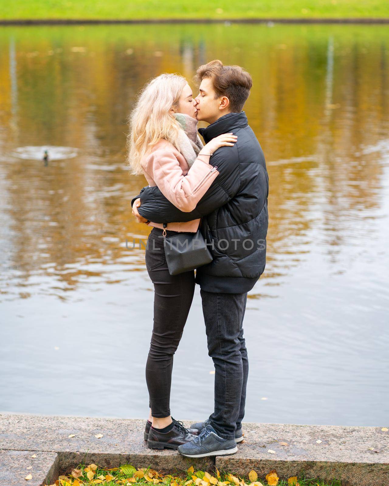 Lovely brunette guy and pretty girl blonde drink coffee and talking on date. Loving teenagers are happy, smiling, kissing. Teen Love Concept. Outdoor, vertical