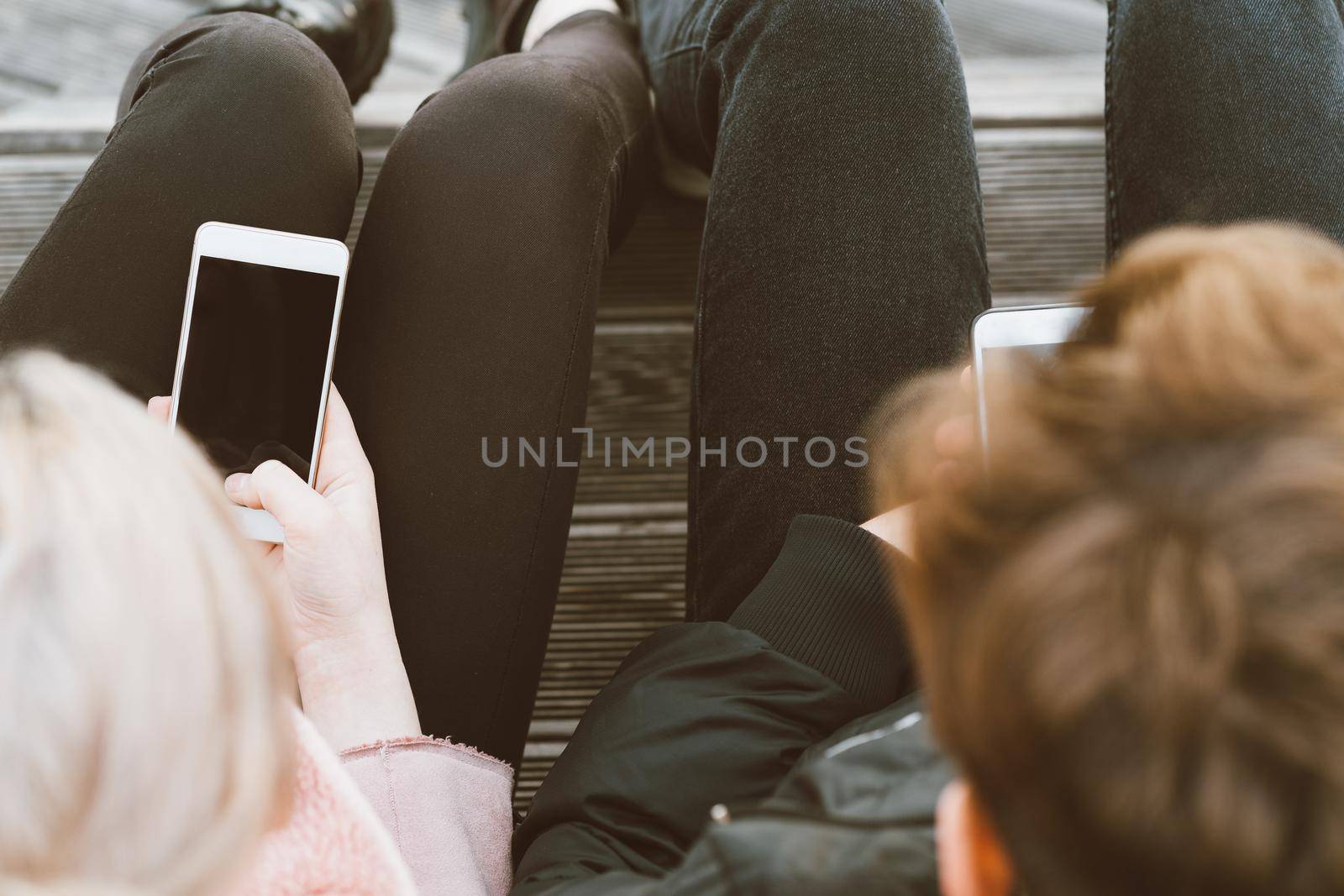 Loving teenagers on date look at mobile phones, sit on park bench in the fall. Immersion in virtual world, social networks. Concept of teenage love, Smombie. Teen dating, top view