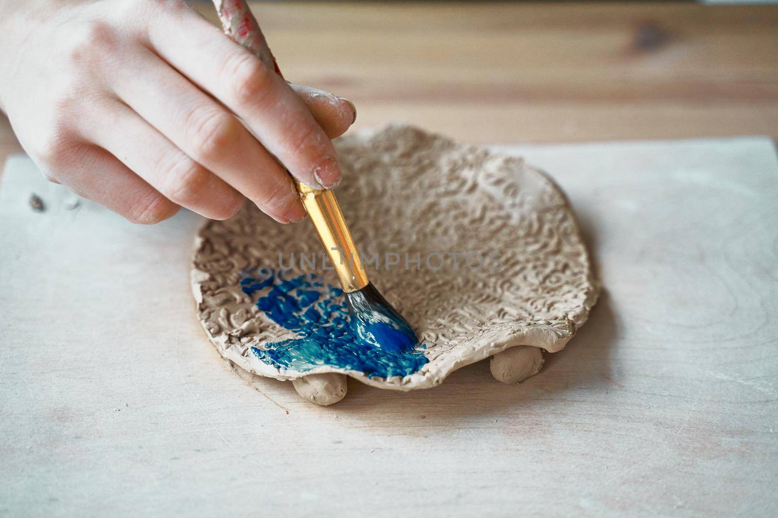 Unrecognised Woman making pattern on ceramic plate, hands close-up, focus on palms with paint brush. Creative hobby concept. Earn extra money, side hustle, turning hobbies into cash, passion into a job