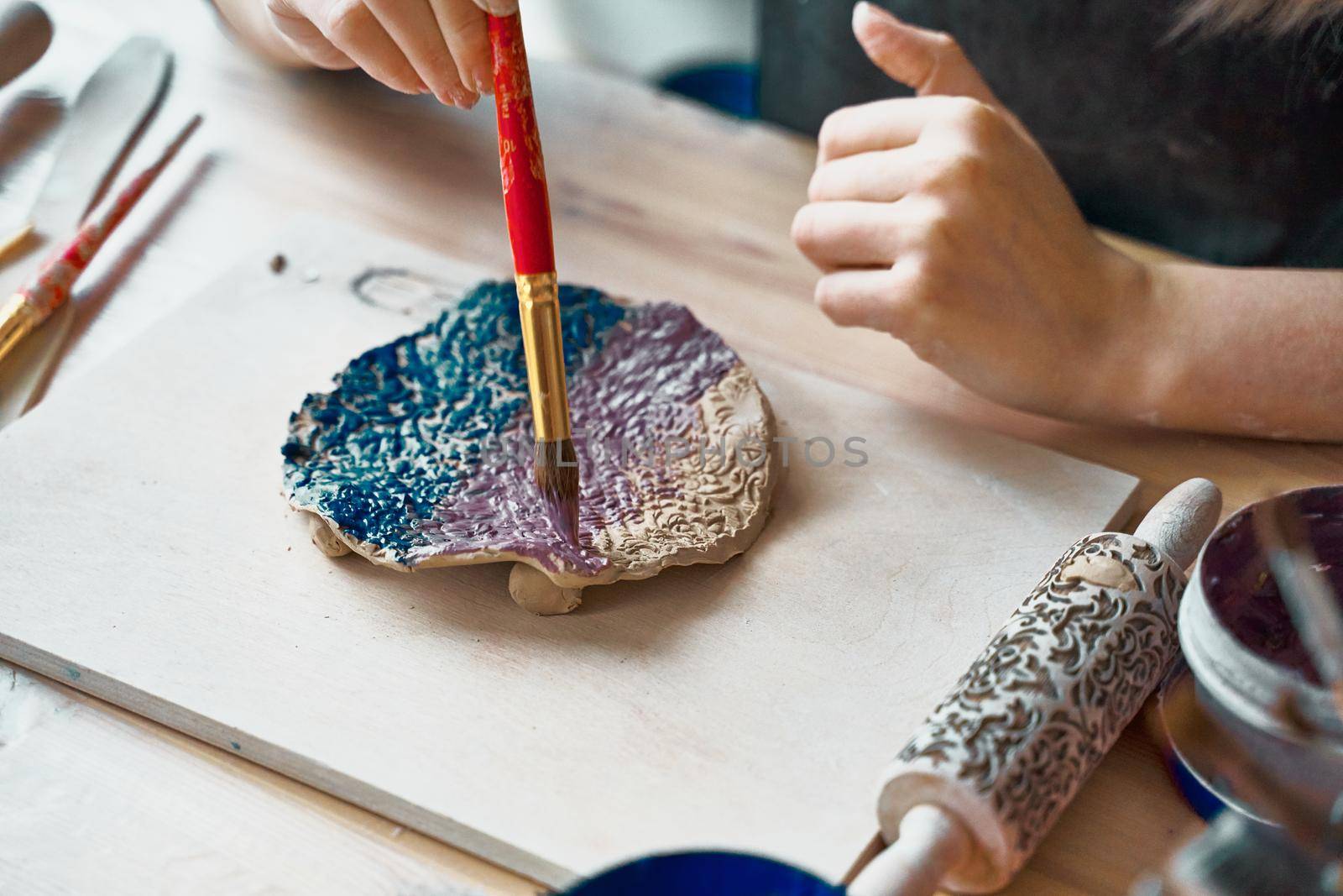 Unrecognised Woman making pattern on ceramic plate, hands close-up, focus on palms with paint brush. Creative hobby concept. Earn extra money, side hustle, turning hobbies into cash, passion into a job