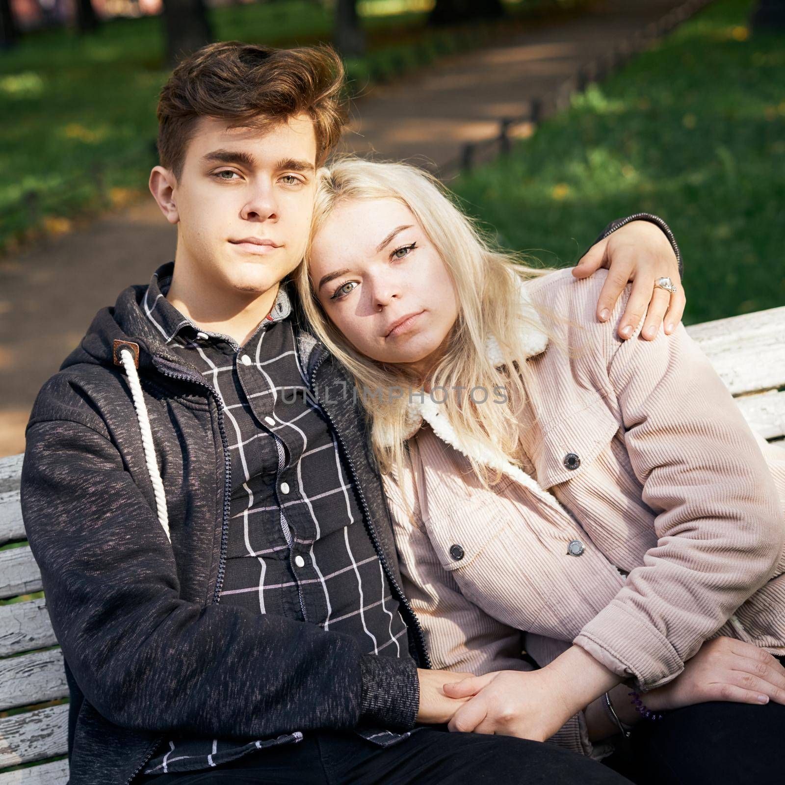 Teenagers in love sit on park bench, resting in the rays of autumn sun, looking straight ahead. Concept of teen love by NataBene