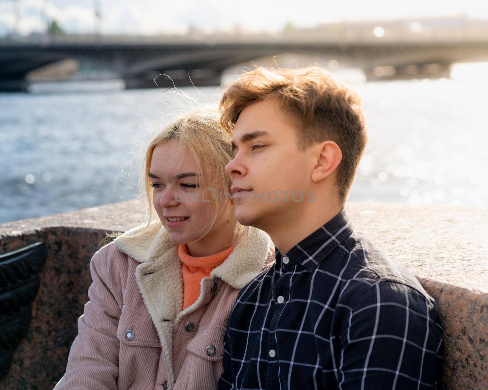 Teenagers in love sit on the waterfront in the city center, resting in the autumn sun. Concept the first teenage love, the beginning of relations. A boy and a girl meet on a date, a couple.