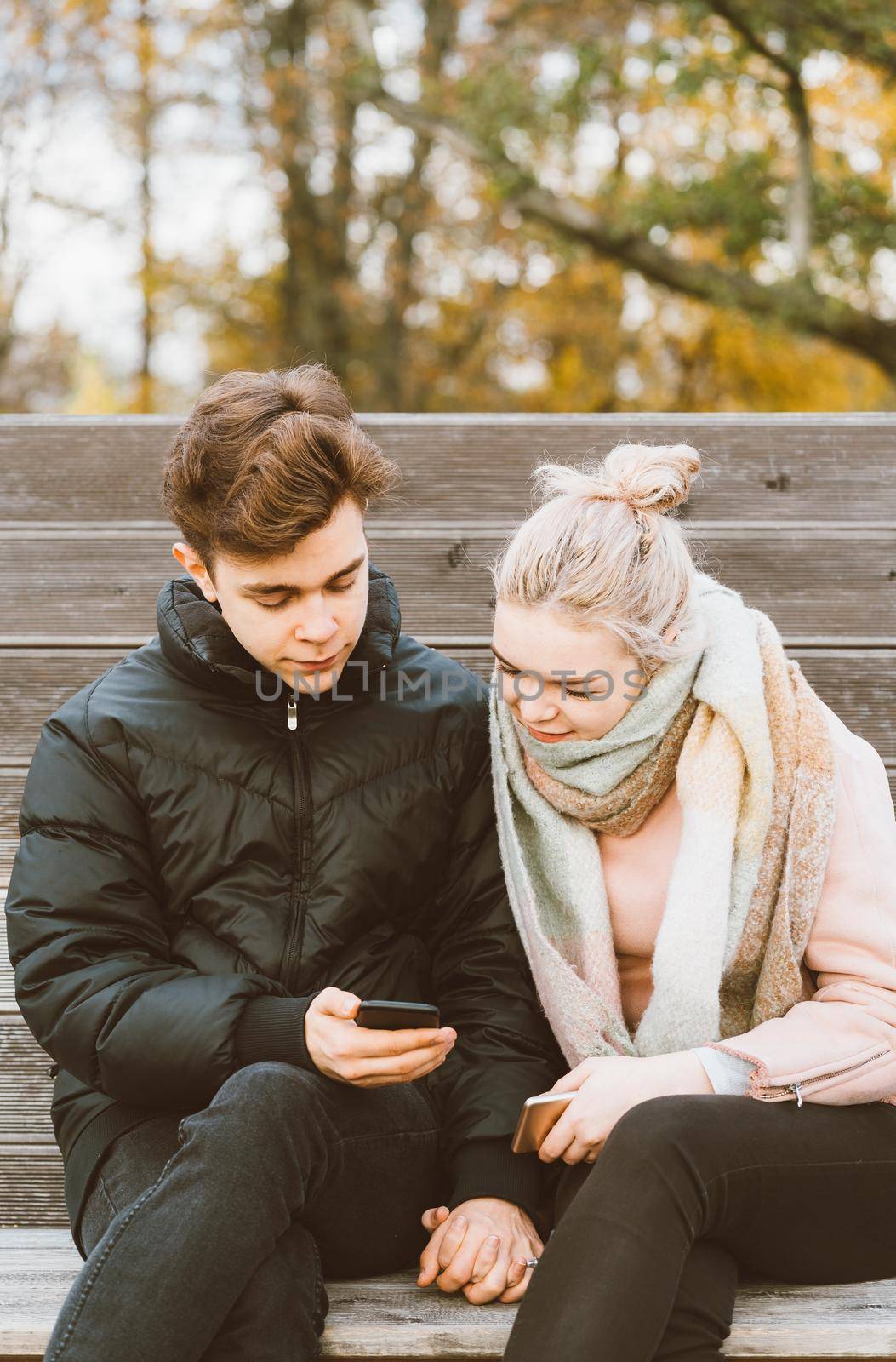 Loving teenagers on date look at mobile phones, guy shows the girl something interesting on the phone. Immersion in virtual world, social networks. Concept of teen love, Smombie dating, vertical