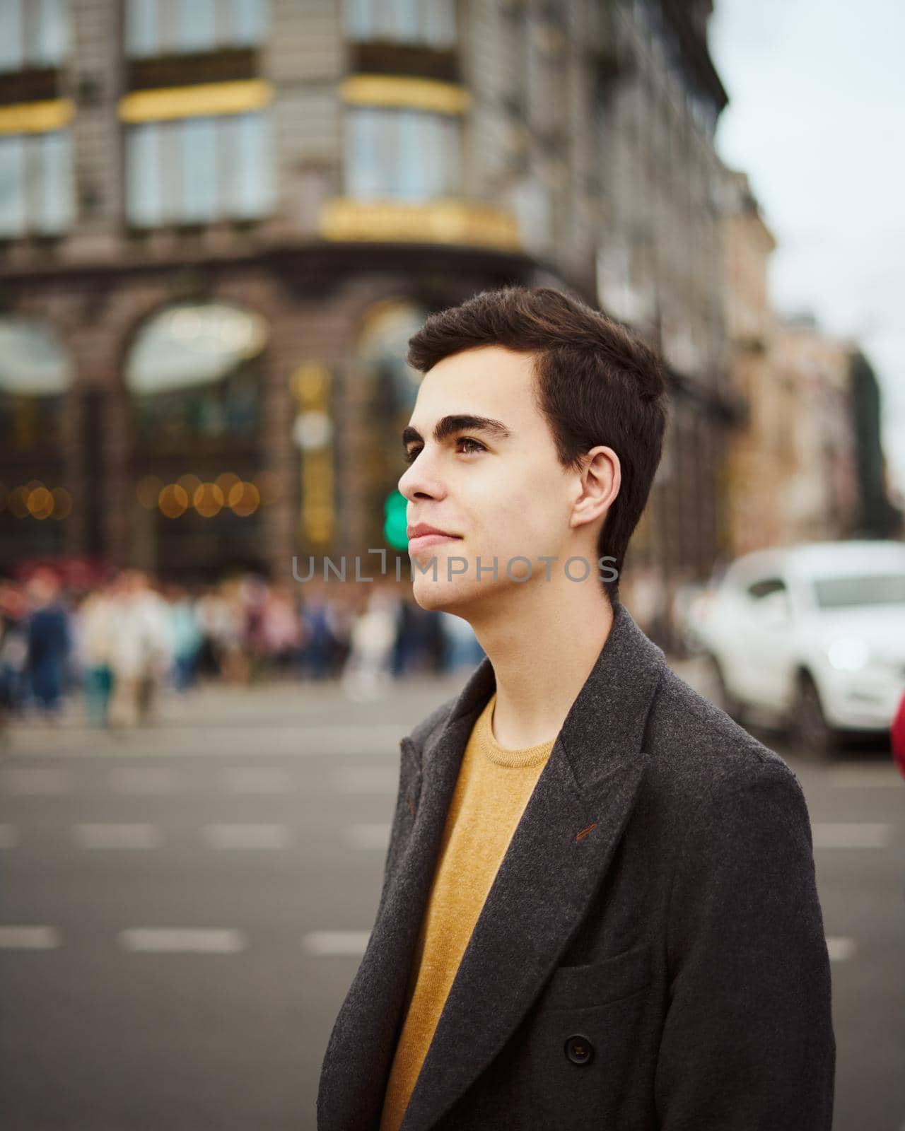 Handsome stylish fashionable man, brunette in elegant gray coat, stands on street in historical center of St. Petersburg. Young man with dark hair, thick eyebrows. by NataBene