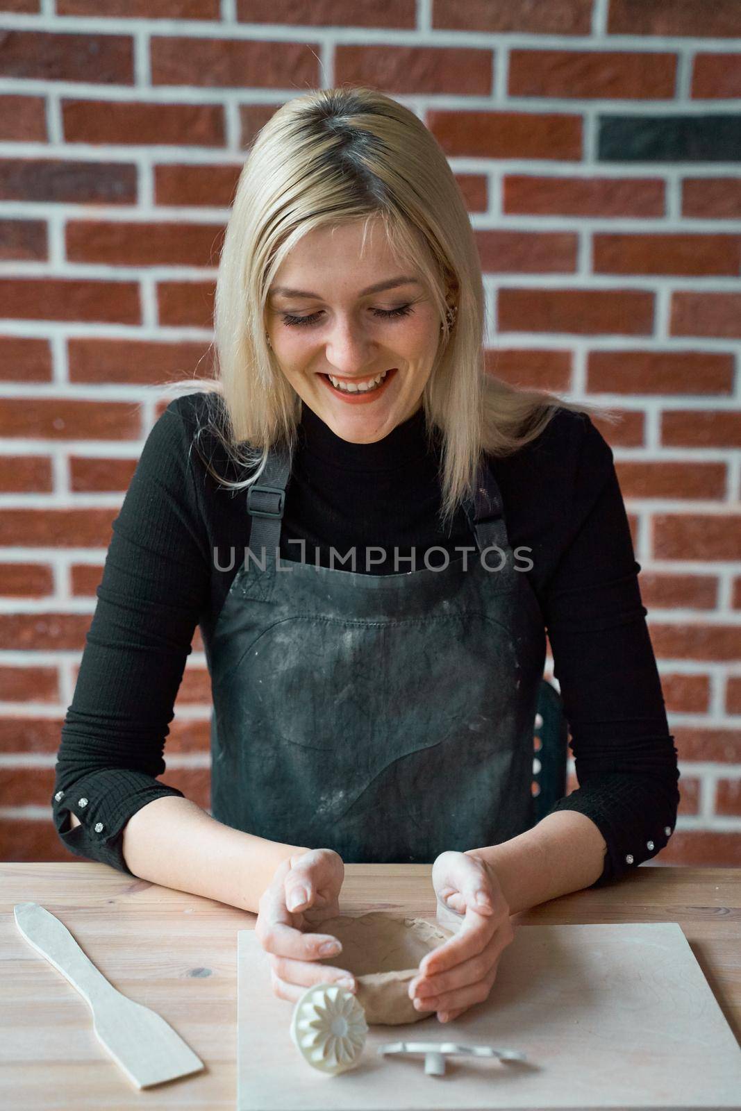 Happy smiling woman making ceramic pottery, tap with spatula. Concept for woman in freelance, business. Handcraft product. Earn extra money, side hustle, turning hobbies into cash, passion into job by NataBene