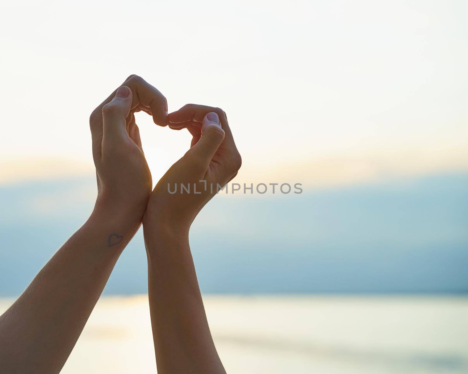 couple showing heart with hands, sign of love, ocean and sunset on background