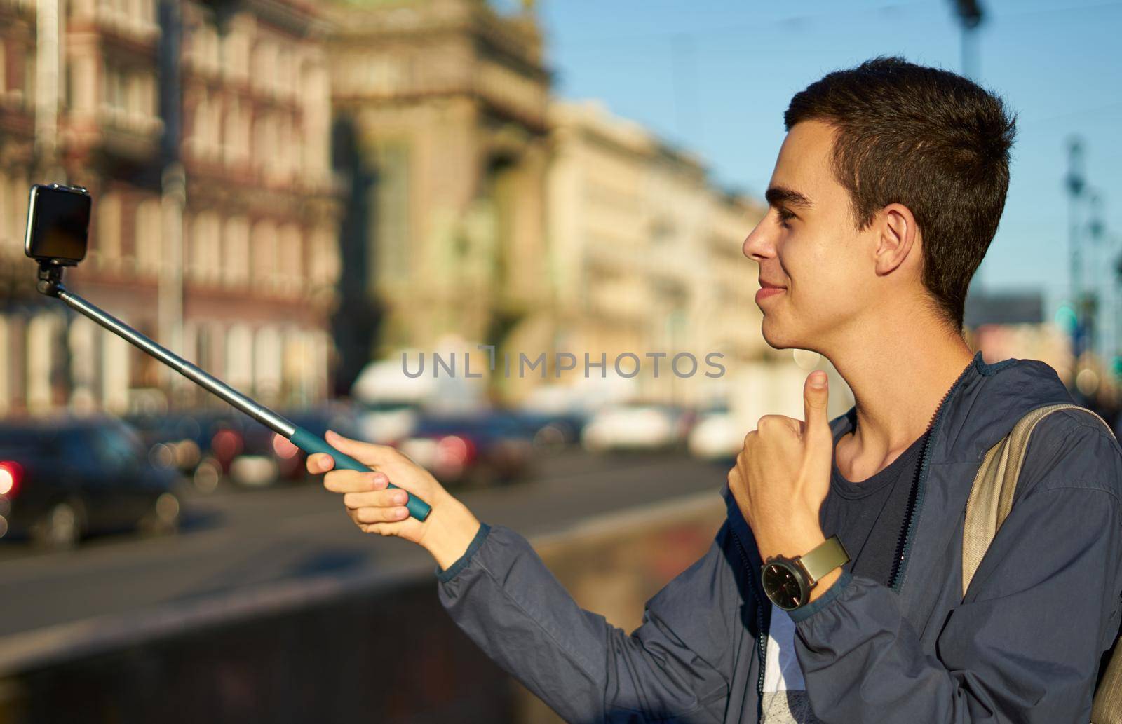 young man with a phone is on the street of a big city and thumbs up, blogger communicates with peoples
