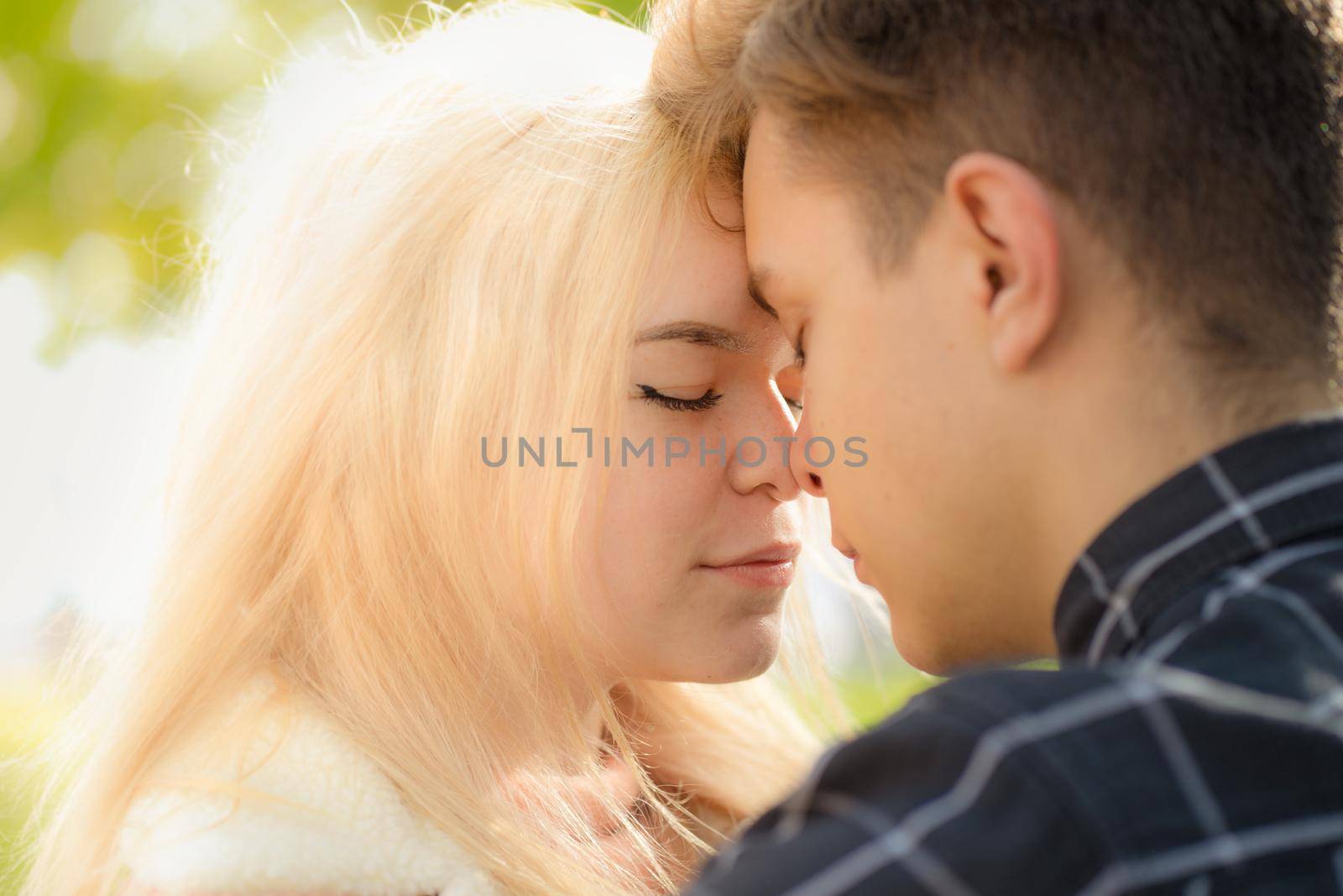 A man affectionately call looks at woman, guy and girl are worth close, touching tips noses. Concept of first teenage love and first kiss. Boy and girl, couple. Intimacy, honesty, trust, open feelings. Close up portrait. by NataBene