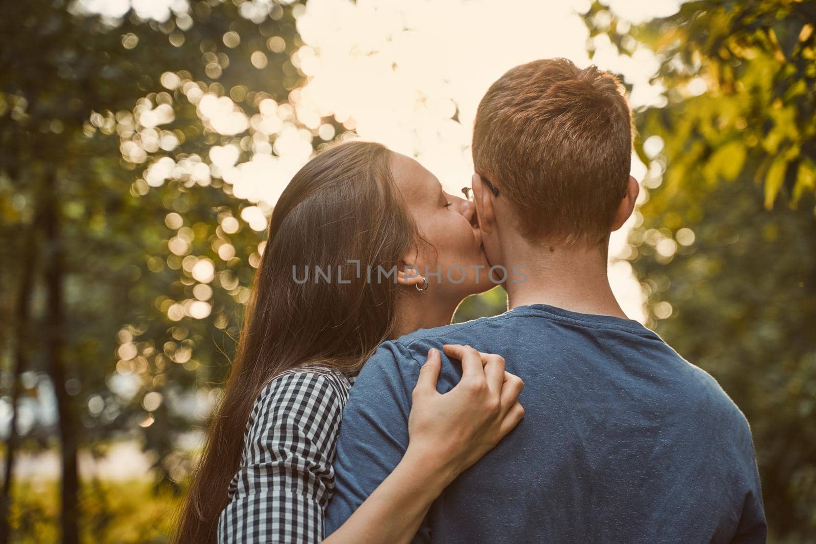 Girl kissing boy in cheek in the park, concept of teen love by NataBene