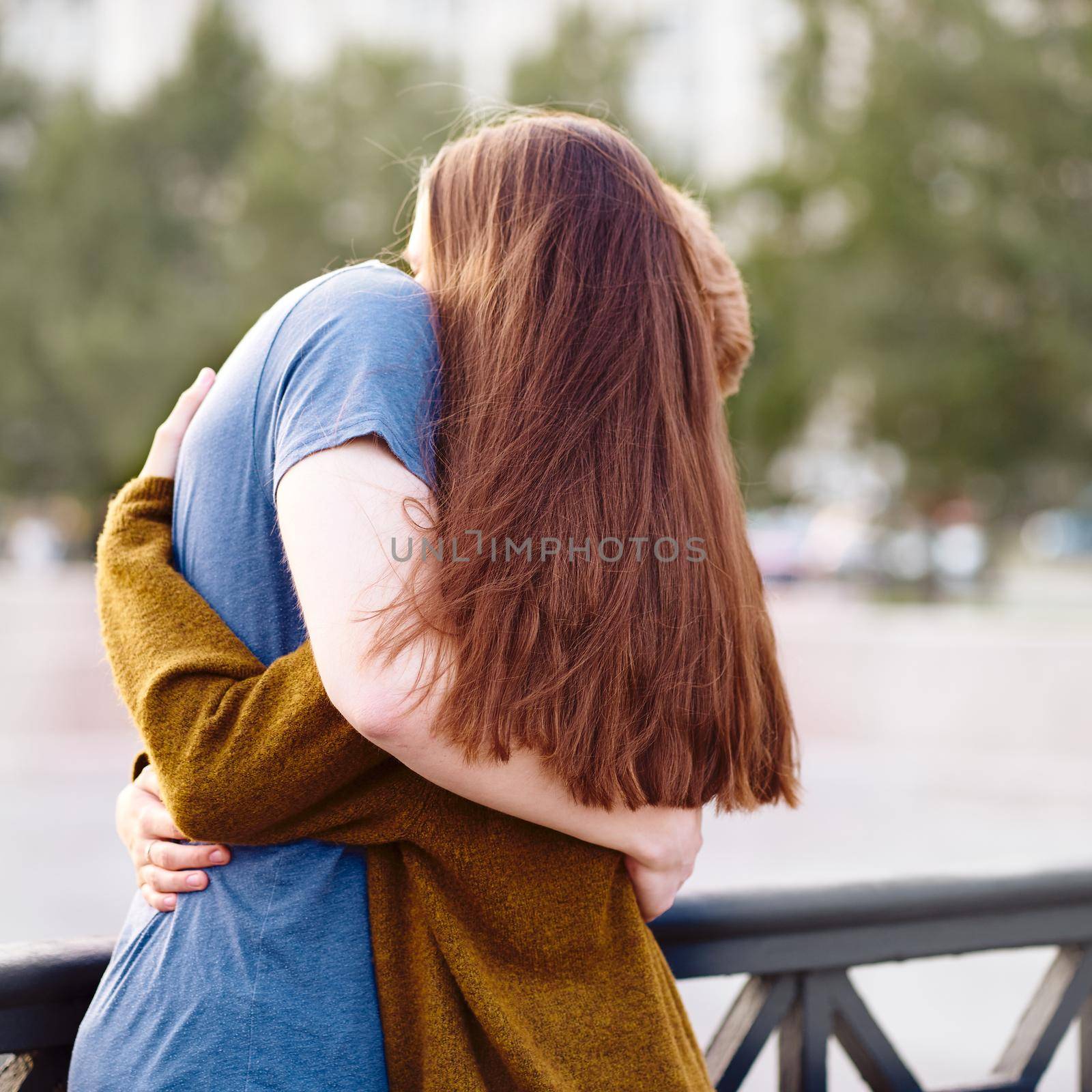 Girl with long thick dark hear embracing redhead boy on bridge, teen love at sunset, summer time