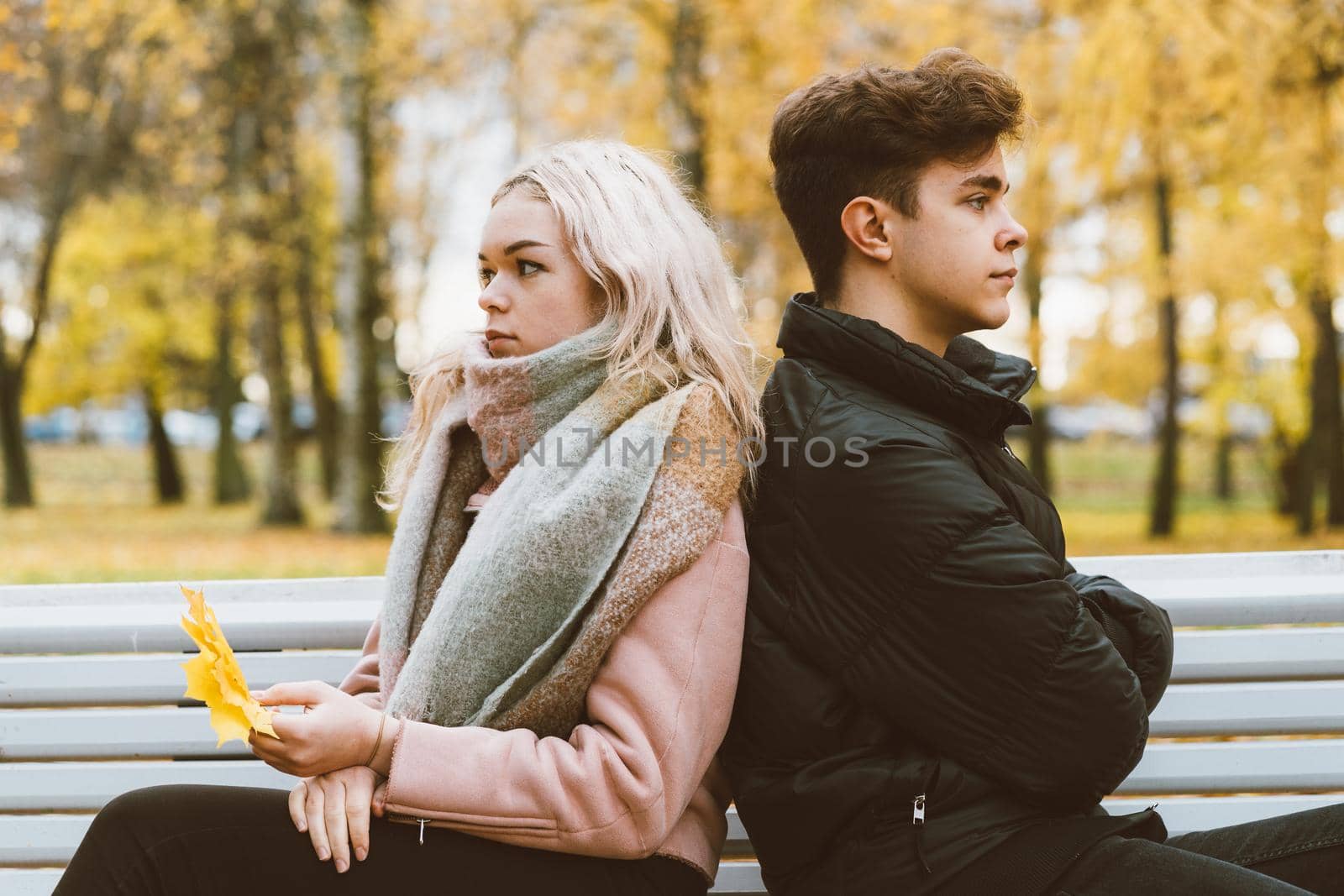 Two teenagers in love in a quarrel. A brunette boy and a blonde girl are sitting on a bench with their backs to each other, do not want to communicate and talk. Teenage Difficulty Concept