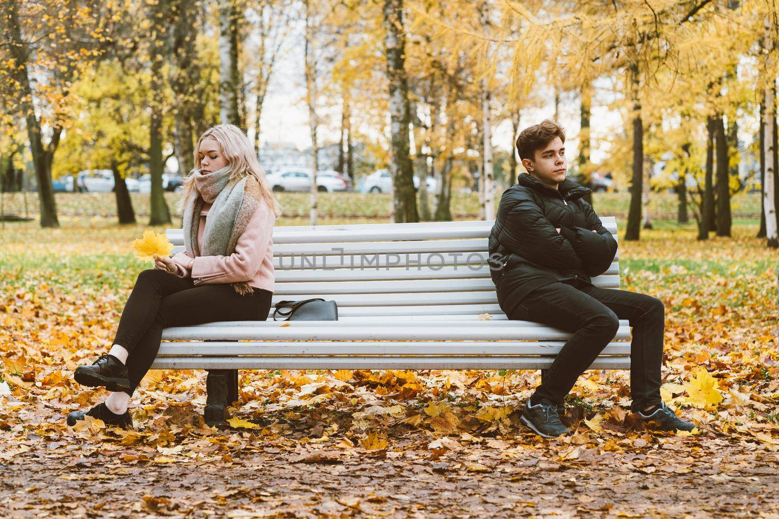 Two teenagers in love in a quarrel. A brunette boy and a blonde girl are sitting on opposite ends of the benches, their backs to each other, do not want to talk and talk. Teenage Difficulty Concept