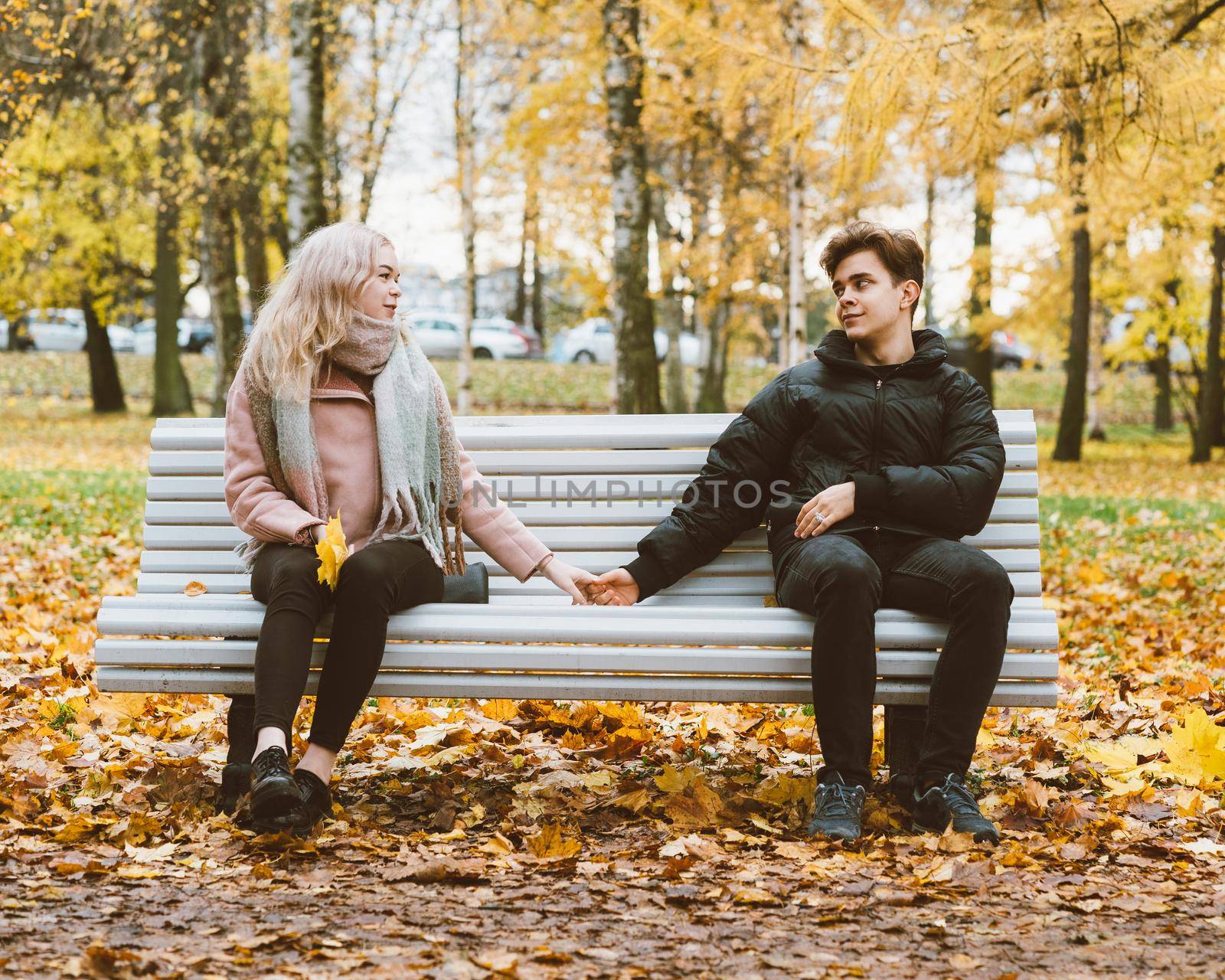 Young beautiful bevushka blonde and a young handsome brunette guy make up after a quarrel. Sitting on a park bench. The concept of teenage love and reconciliation