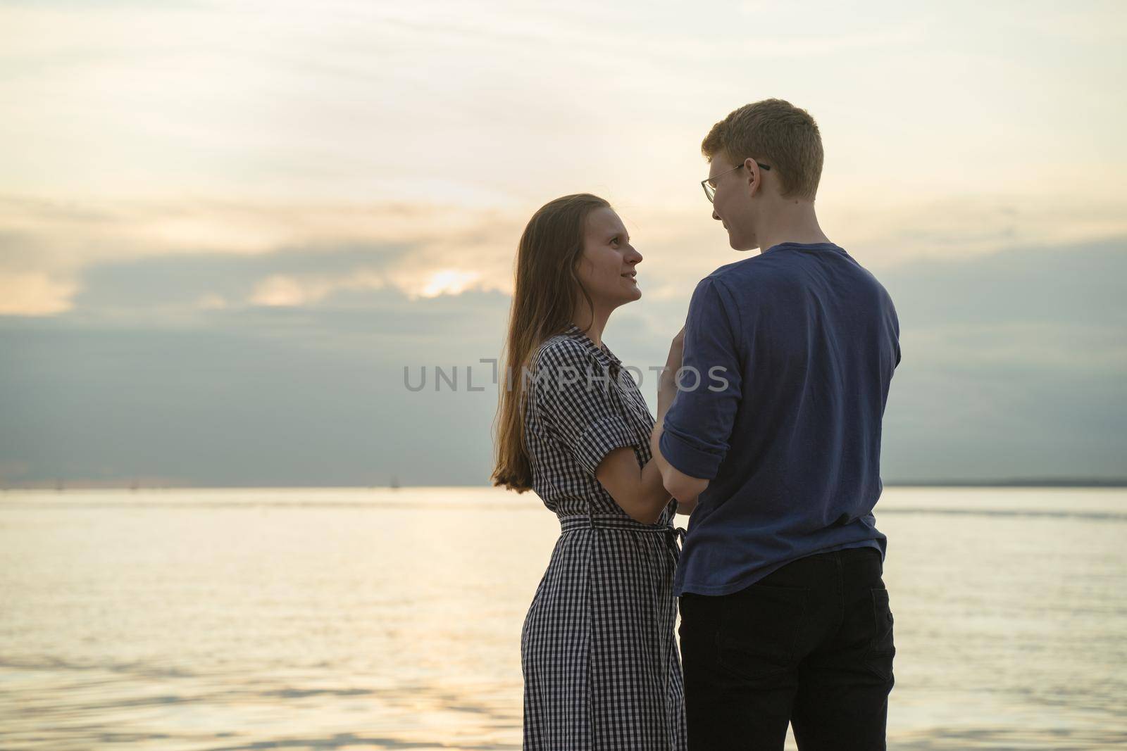 teen couple, ocean clouds and sunset on background, girl looking at boy and smiling