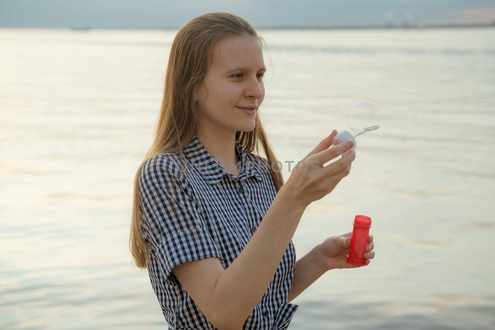 teenager blowing soup bubbles, beach on background, closeup, side view