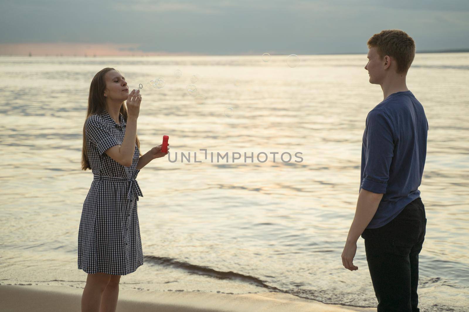 teen couple having fun on beach, girl blow bubbles and boy standing next to her