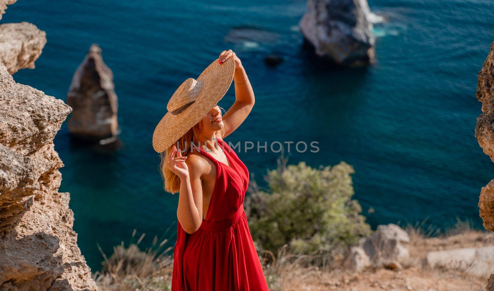 A woman in a flying red dress fluttering in the wind and a straw hat against the backdrop of the sea. by Matiunina