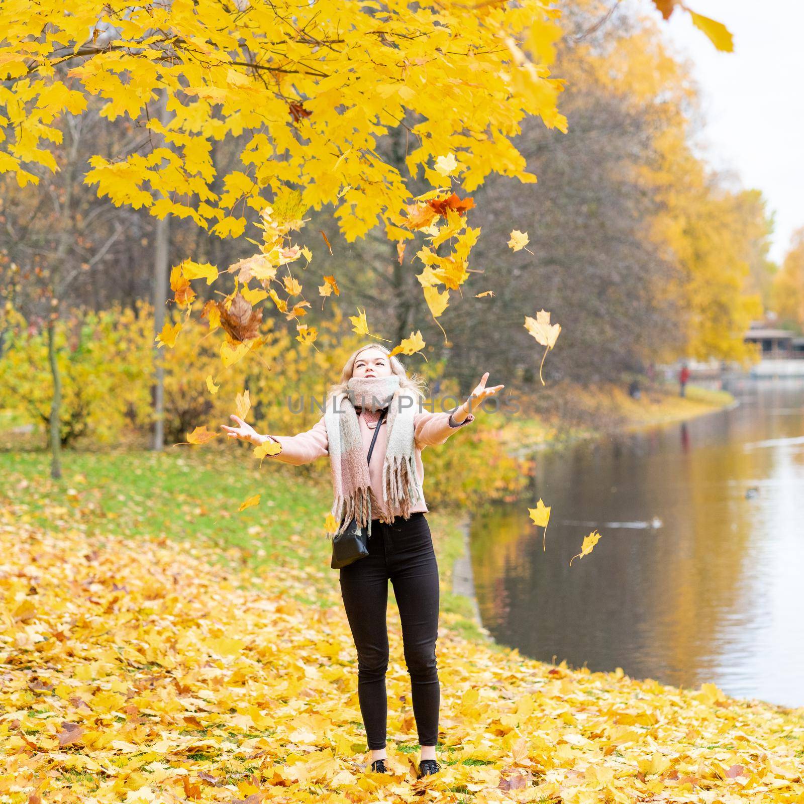 Beautiful young girl throws up autumn leaves. Attractive young woman is resting, fooling around, playing with leaves in a park.