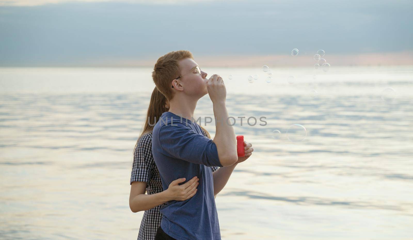 Teen Couple blowing soup bubbles on the beach, ocean and sky on background by NataBene